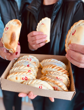 Manos sosteniendo empanadas recién horneadas de Casa Pueblo, con una caja llena de fondo